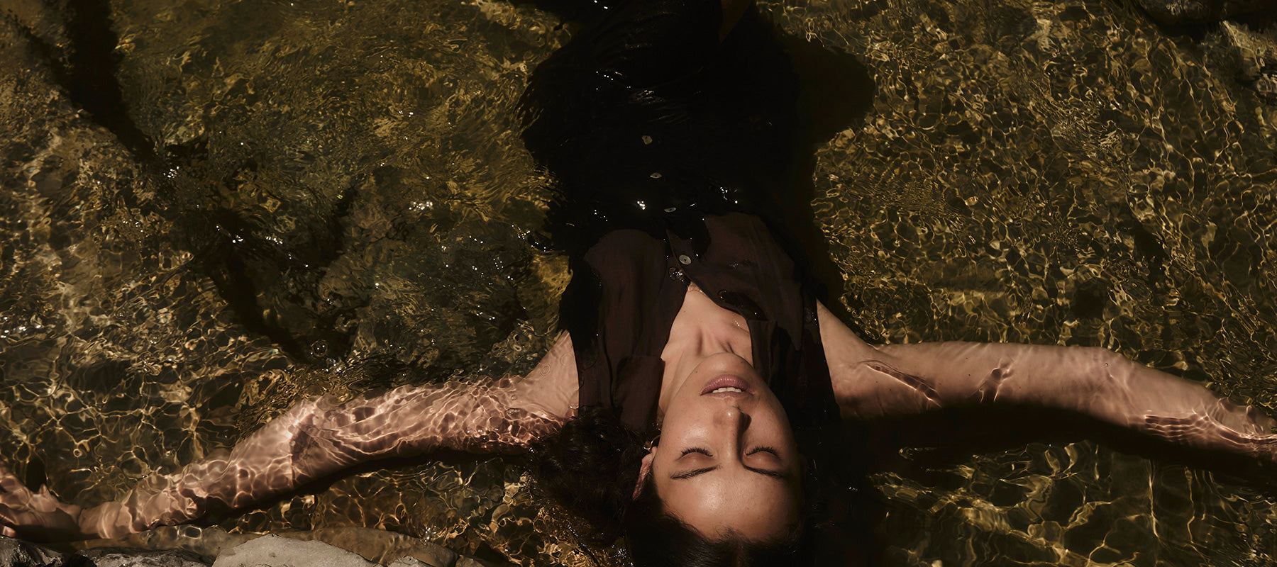 Woman with dark brown dress lies in water with closed eyes
